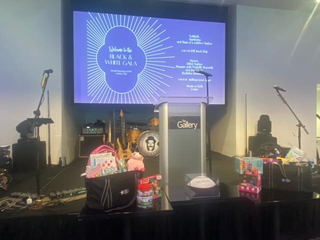 The stage with microphones, the speakers podium, a large screen with event information on it, musical instruments, and bags of toys.