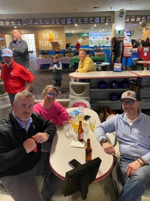 3 people sitting at their table at their bowling lane. They are smiling for the camera.