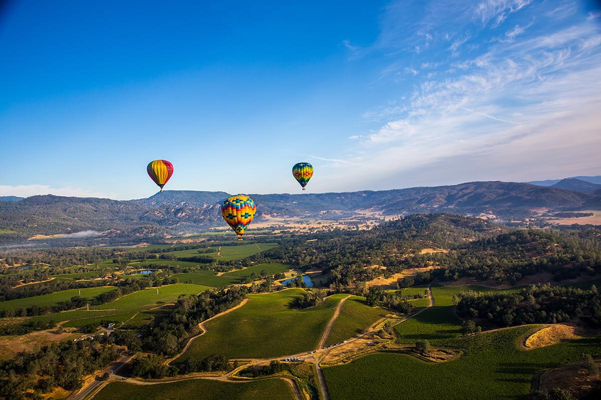 A birds eye view of the Napa Valley with 3 hot air balloons in the sky.
