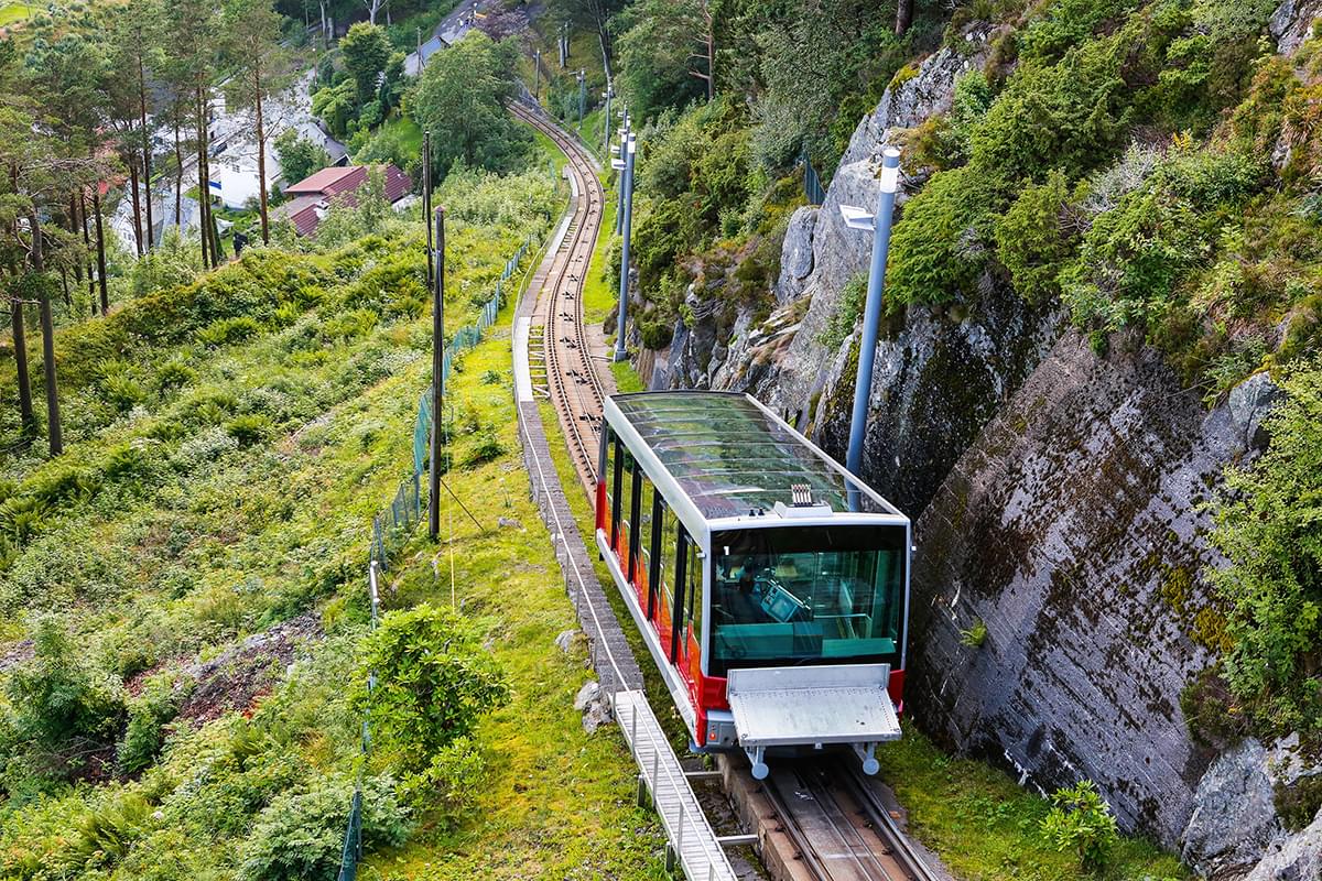 a tram on a track going through a grassy area with one side against the edge of a grassy mountain.
