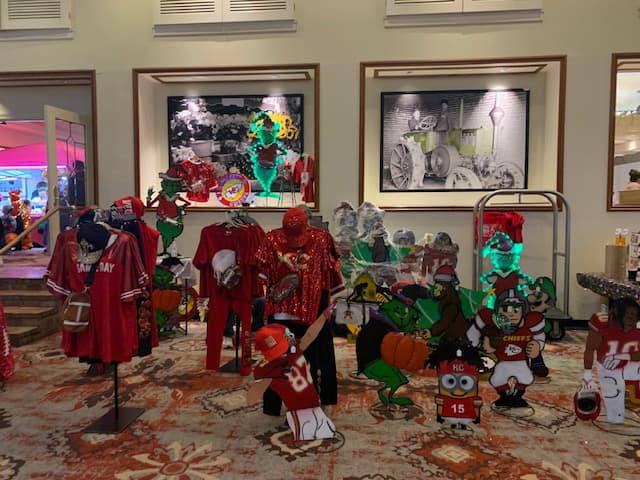 Red football clothing, football lawn ornaments, and Christmas lawn ornaments lined up inside a large ornate room.